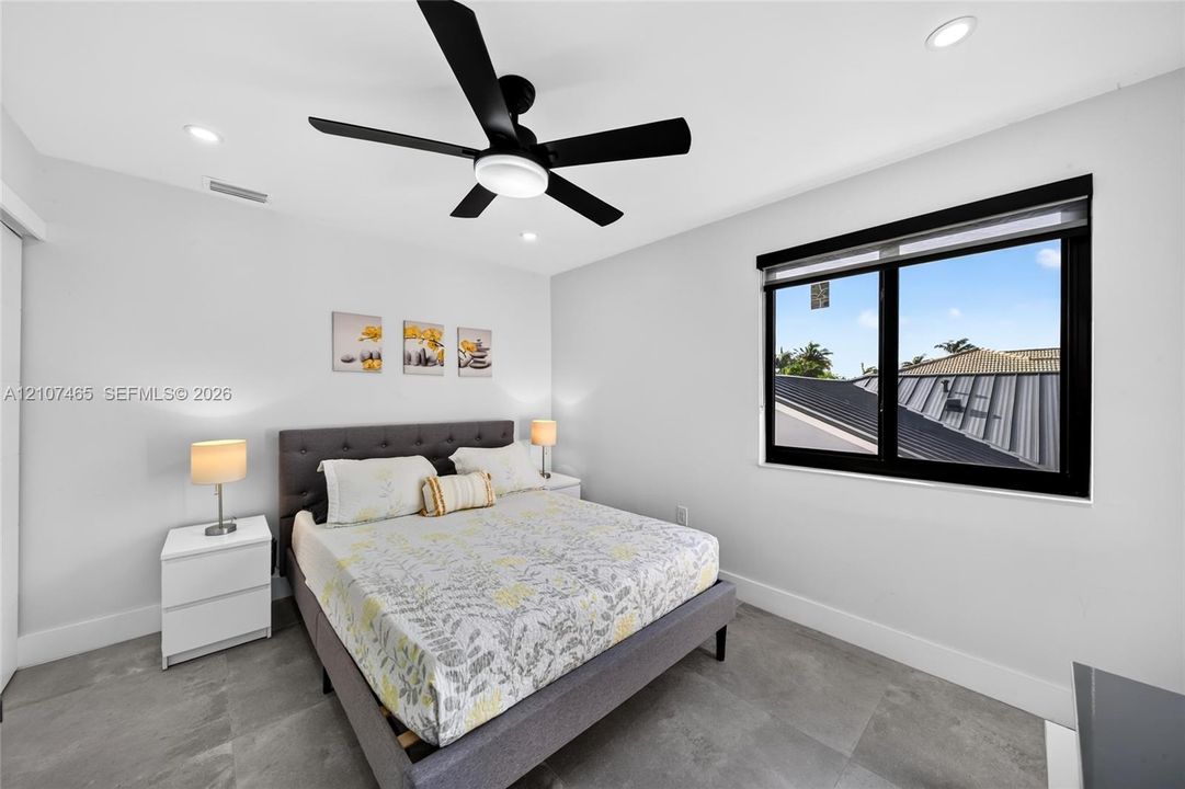 Large-format tile flooring, recessed ceiling lighting, matte black ceiling fan, and window with black frame