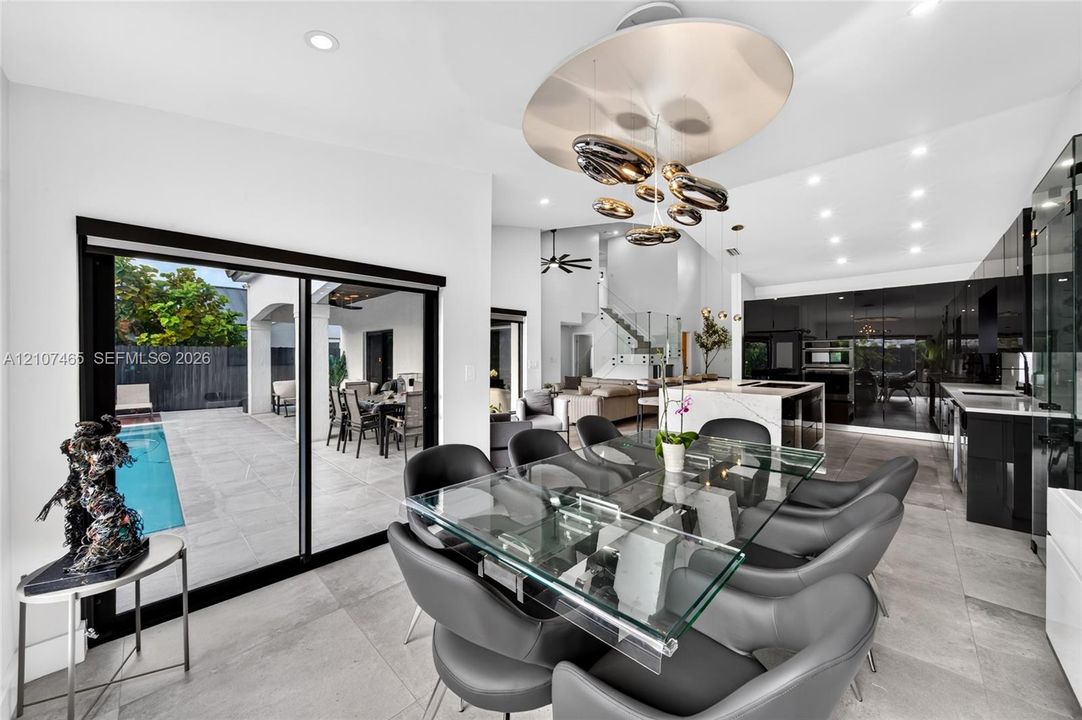 Open-concept space featuring large-format stone tile flooring, high-gloss cabinetry, a central kitchen island with stone countertops, and floor-to-ceiling sliding glass doors