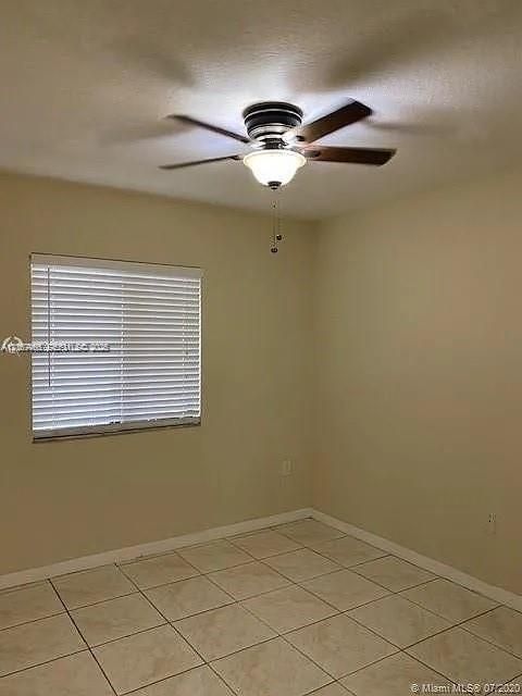 Neutral-toned interior space featuring light-colored ceramic tile flooring, a multi-blade ceiling fan with an integrated light fixture, and horizontal window blinds