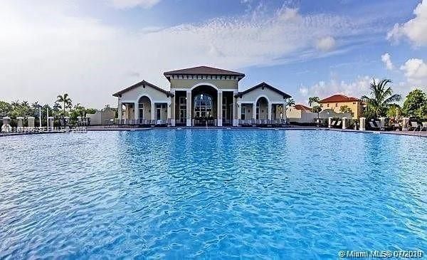 Expansive swimming pool with integrated hardscaping and Mediterranean-inspired clubhouse featuring arched entryways and a multi-gabled roofline