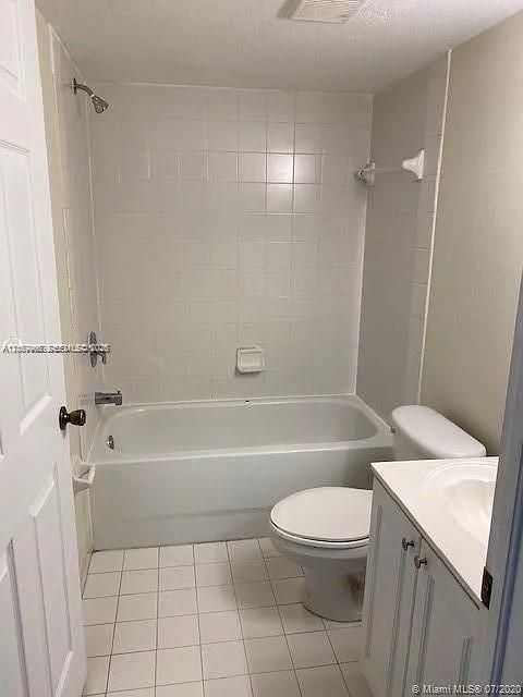 Full bathroom featuring white tile flooring, a tub-shower combination with white wall tile surround, a built-in soap dish, and a white vanity cabinet