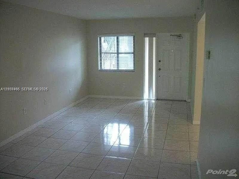 Neutral-toned interior space featuring light-colored tile flooring, a window with horizontal blinds, and a paneled entry door with an integrated sidelight