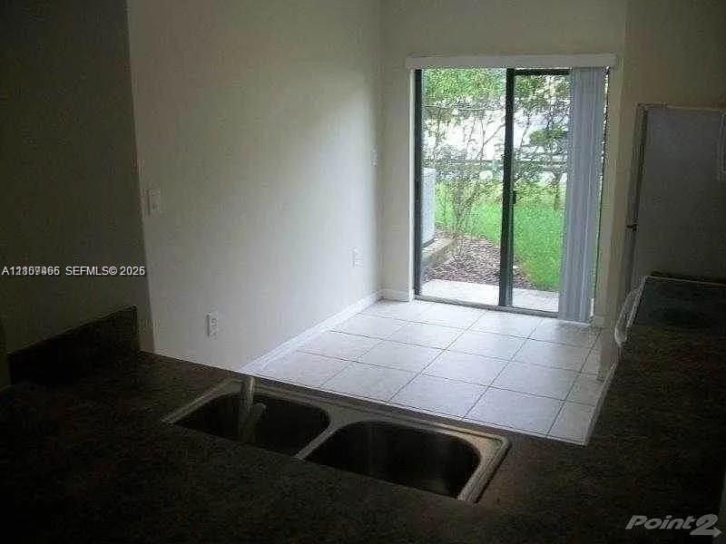 Kitchen area featuring a stone-surface countertop, double-basin stainless steel sink, ceramic tile flooring, and a sliding glass door