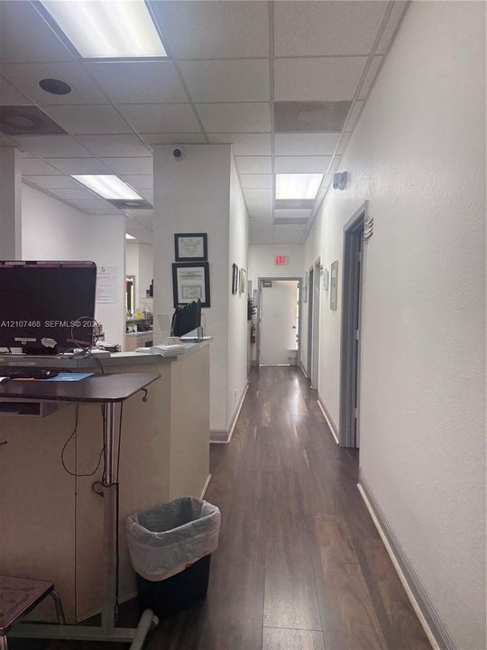 Hallway with wood-finish flooring, fluorescent overhead lighting, and multiple interior doors