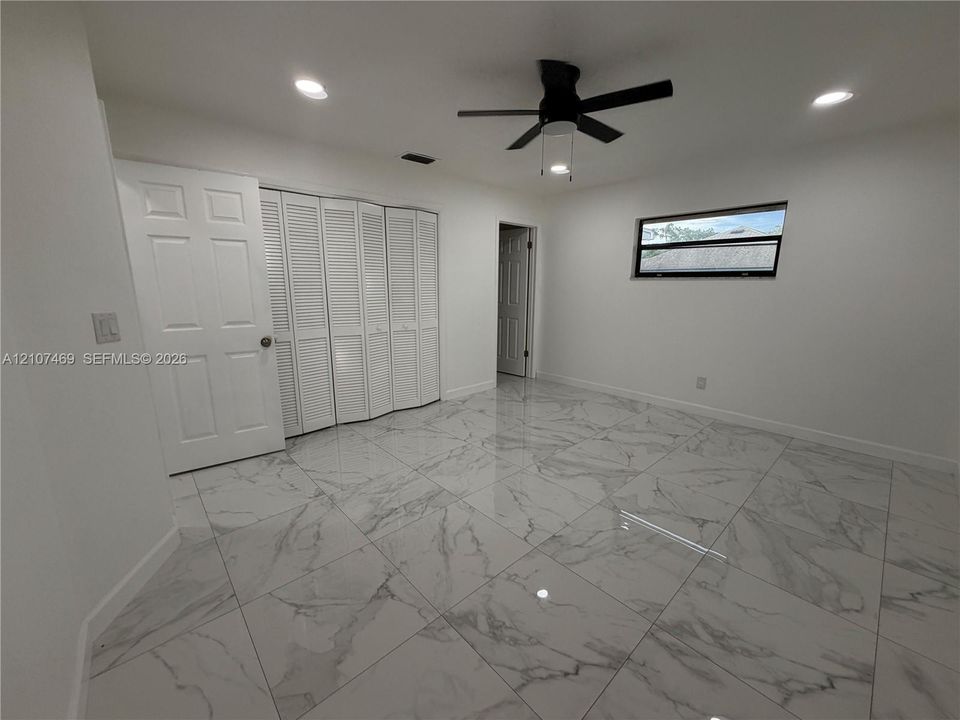 Large-format stone-finish tile flooring, white bi-fold closet doors, recessed ceiling lighting, and a multi-blade ceiling fan