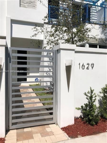 Contemporary exterior featuring a gated entry with horizontal metal slats, stone paver walkway, stucco finish wall, and geometric wall-mounted lighting