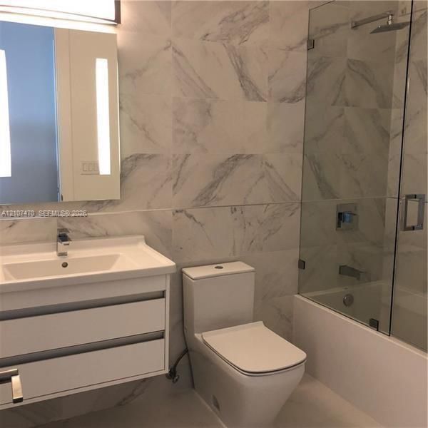 Wall-mounted floating vanity with integrated rectangular sink, large-format veined tile wall surfacing, glass-enclosed shower, polished chrome fixtures, and integrated vanity lighting
