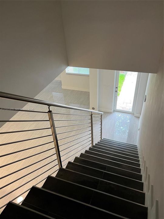 Staircase featuring dark tile treads, a stainless steel cable railing system, polished large-format floor tile, and a glass-paneled entry door