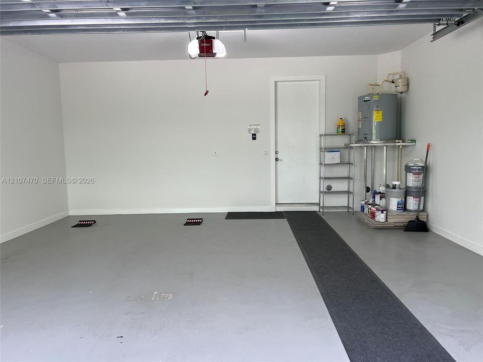 Finished garage featuring grey epoxy flooring, neutral wall paint, overhead door opener, and a dedicated utility area with a water heater