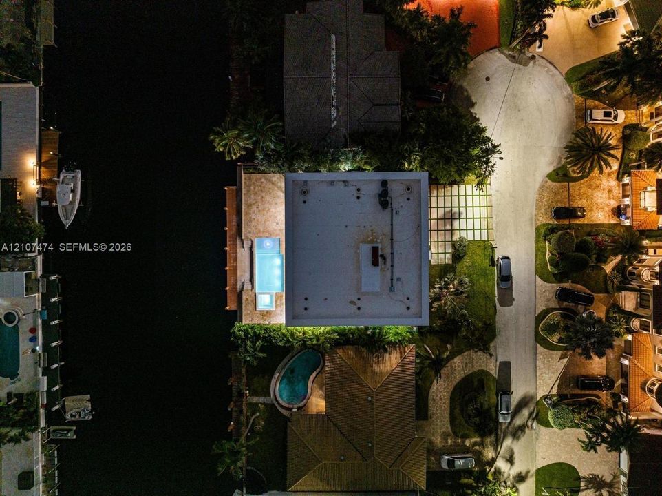Aerial perspective of waterfront property featuring a deep-water dock, integrated swimming pool, paved driveway, and established landscaping