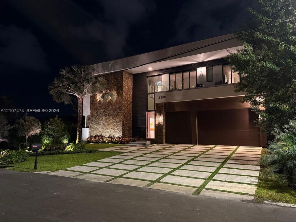 Contemporary exterior featuring textured stone masonry, a two-car garage, multi-level glass balcony railings, and a geometric concrete paver driveway