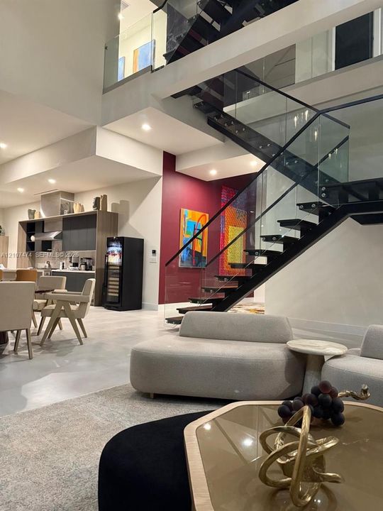 Open-concept interior featuring a glass and black metal floating staircase, recessed lighting, polished concrete flooring, and high ceilings
