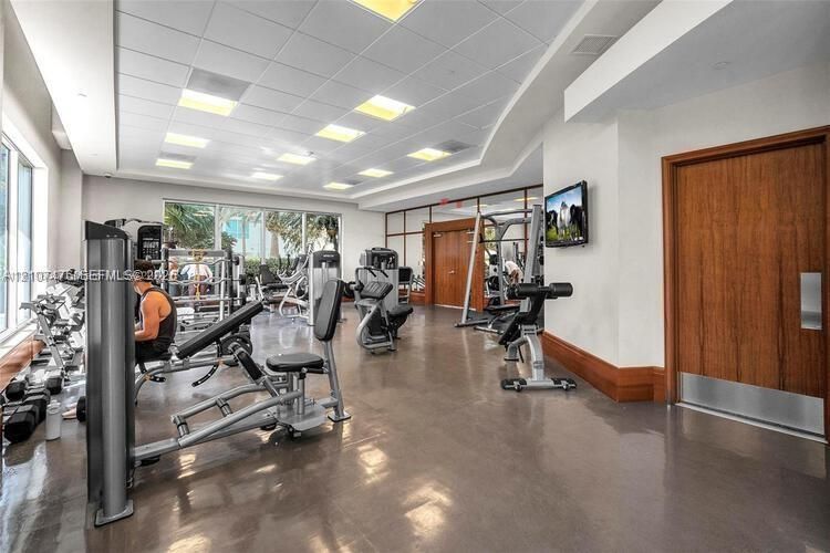 Fitness center featuring a drop ceiling with recessed lighting, large-format floor tiling, extensive floor-to-ceiling windows, and wood-finish door with a metal kick plate