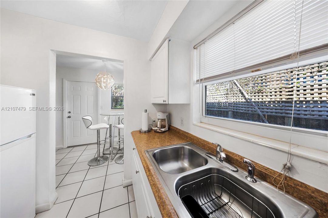 Cottage guest house, Kitchen featuring white cabinetry, stone-finish countertops, a double-basin stainless steel sink with a high-arch faucet, and tile flooring