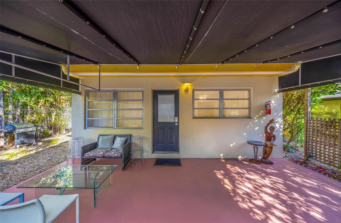 Cottage guest house Entrance, Covered patio featuring a solid-surface floor, retractable black fabric awning, horizontal sliding windows, and a glass-paneled exterior door