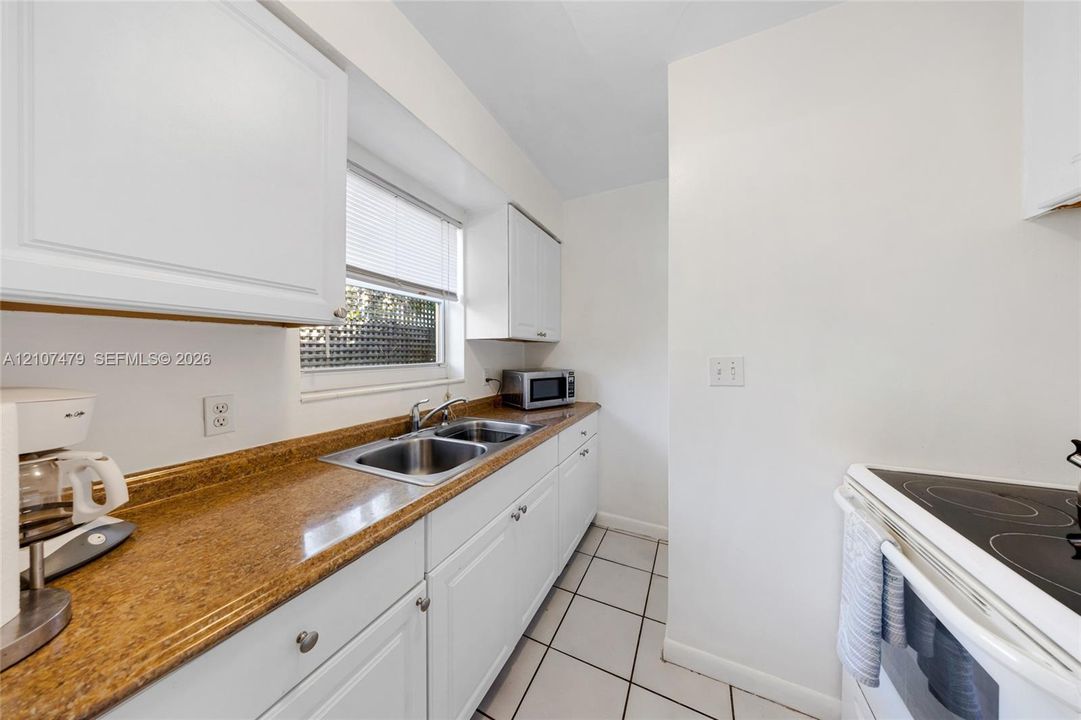 Cottage guest house, Kitchen featuring white shaker-style cabinetry, solid-surface countertops, dual-basin stainless steel sink, and ceramic tile flooring