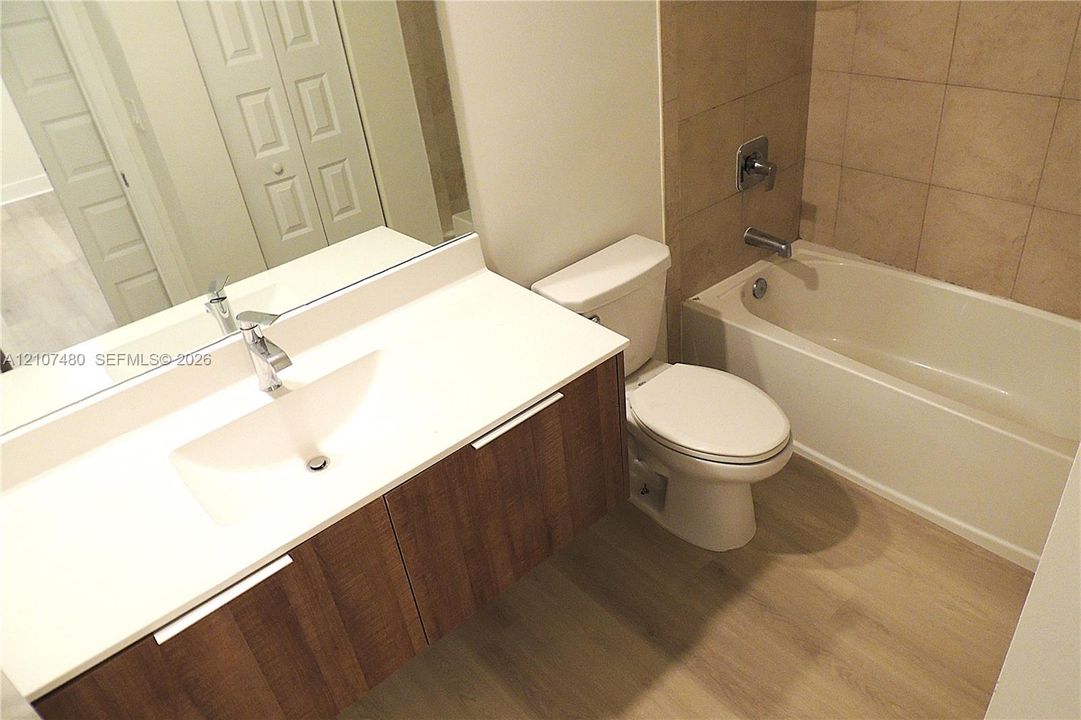 Floating wood-finish vanity with an integrated basin, white solid-surface countertop, full-width mirror, and neutral-toned tile shower surround