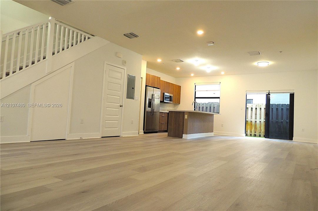 Open floor plan featuring wood-finish flooring, recessed lighting, a central kitchen island, wood-finish cabinetry, and a staircase with a white railing