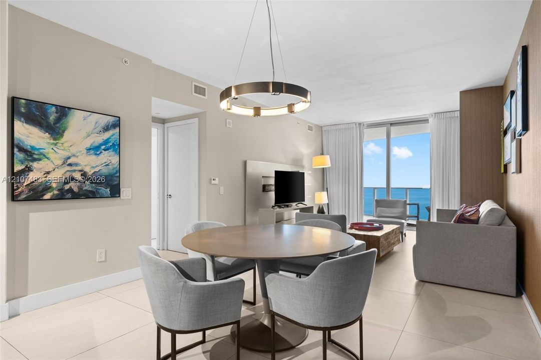 Large format neutral tile flooring, circular modern pendant lighting, and floor-to-ceiling glass sliding doors opening to a balcony with ocean scenery