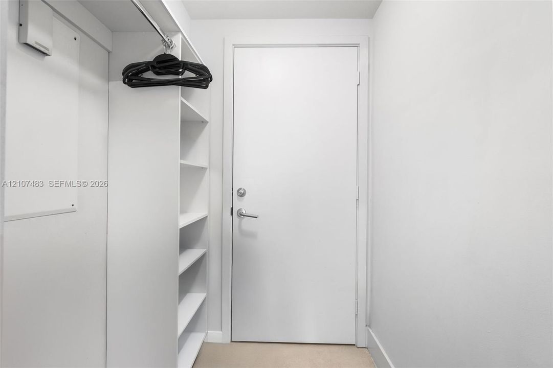 Storage area featuring built-in white shelving, a metal garment rod, and a solid-core interior door with satin-finish hardware