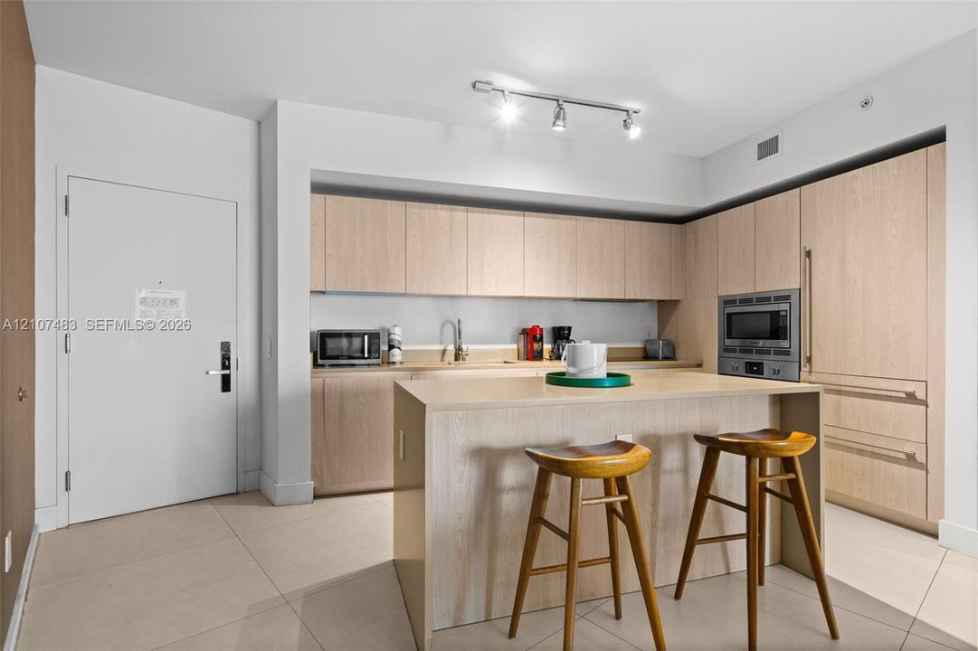 Kitchen featuring light-toned cabinetry, a built-in oven, large-format tile flooring, a center island with counter seating, and track lighting