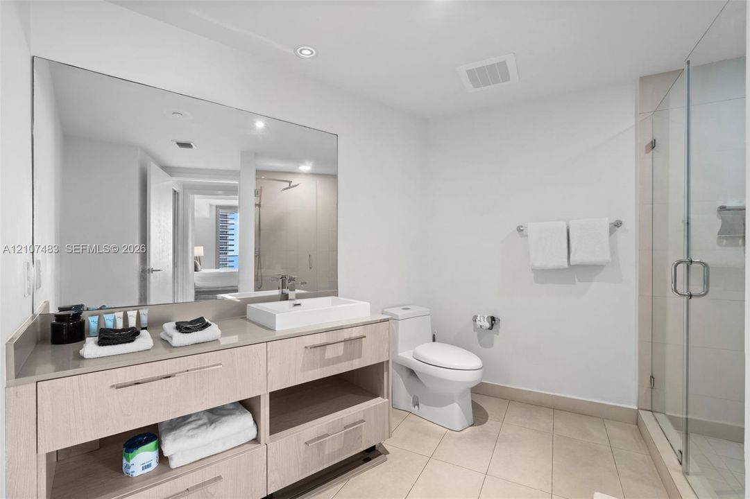 Modern bathroom featuring a wood-finish vanity with a rectangular vessel sink, quartz countertop, large wall-mounted mirror, and a glass-enclosed shower with tiled walls