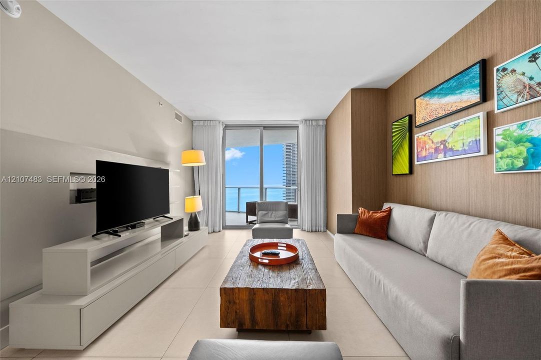 Living space featuring floor-to-ceiling sliding glass doors, neutral tile flooring, a custom wood-paneled accent wall, and a built-in media console
