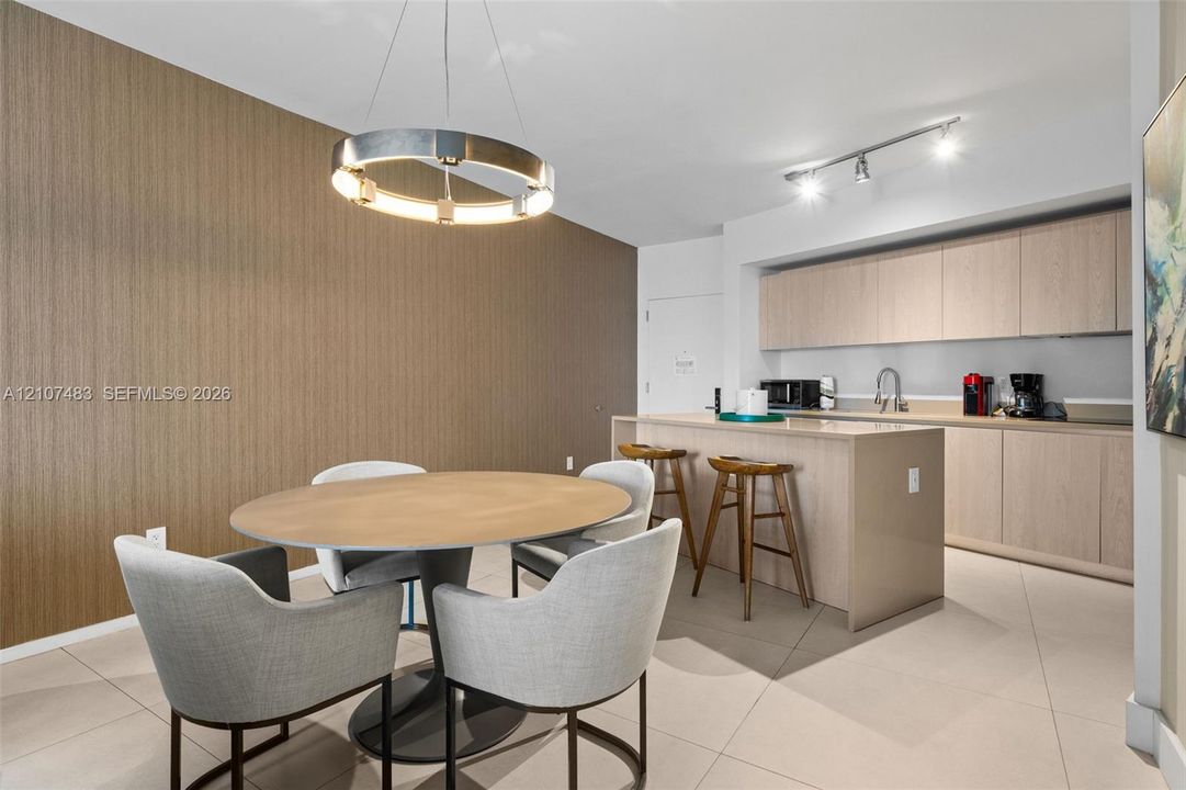 Kitchen featuring light-toned wood cabinetry, stone-surface island, tile flooring, modern circular statement pendant light, and track lighting