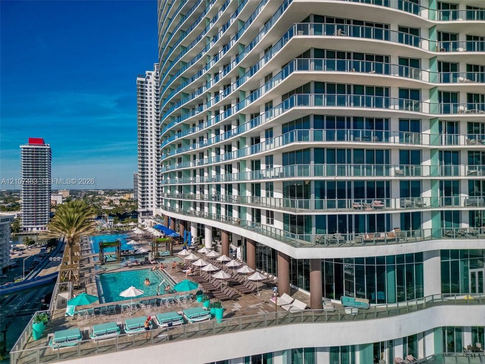 High-rise architecture featuring tiered, wrap-around glass balconies, expansive floor-to-ceiling windows, and a multi-level pool deck with built-in stone hardscaping
