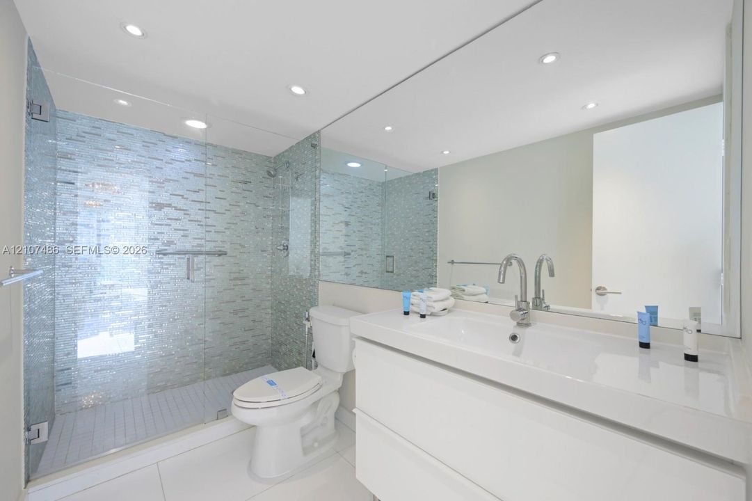 Walk-in shower with glass enclosure and mosaic tile surround, white floating vanity with integrated basin, polished chrome faucet, and expansive wall-to-wall mirror
