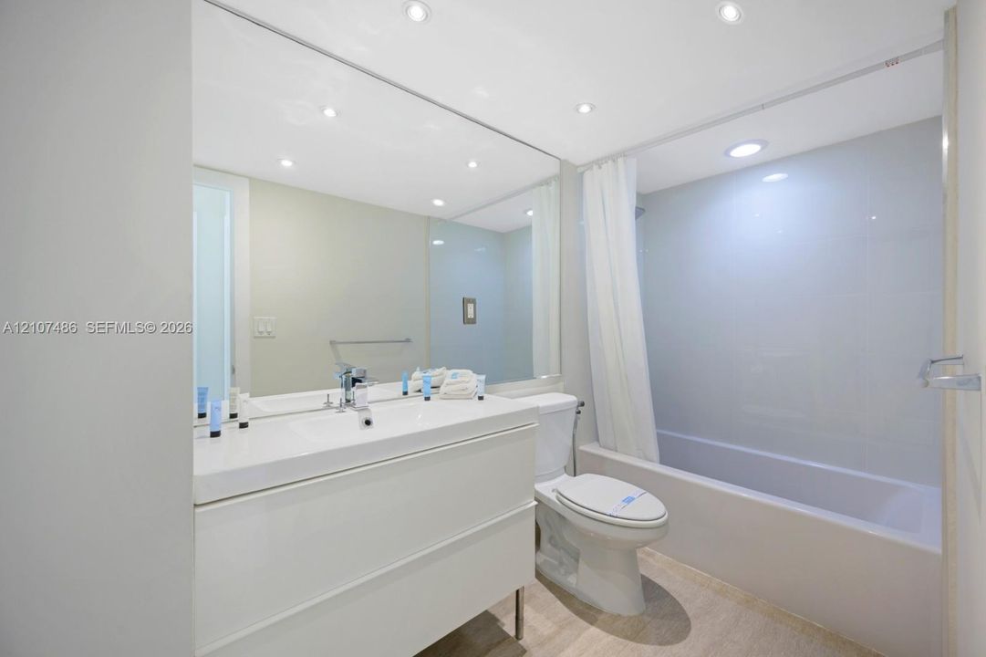 Modern white vanity with a rectangular sink, expansive wall-to-wall mirror, recessed ceiling lighting, and a full-height tile surround in the shower-tub combination