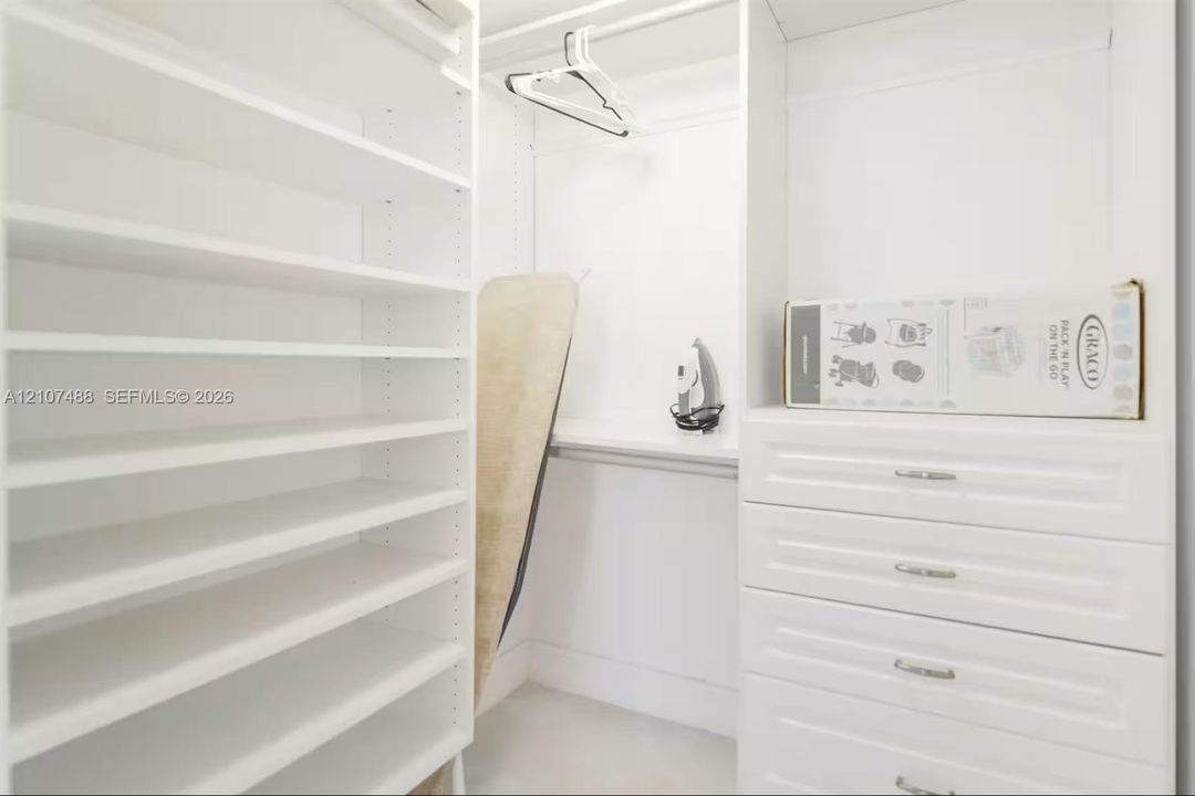 Custom built-in closet featuring white cabinetry, floor-to-ceiling adjustable shelving, integrated storage drawers with metal hardware, and overhead hanging rods