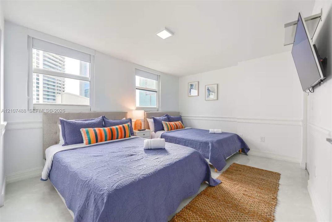 Neutral-toned room featuring high-gloss flooring, horizontal chair rail molding, dual large-format windows, and square LED ceiling lighting