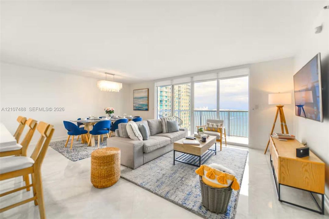 Open-concept main living area featuring light-toned tile flooring, floor-to-ceiling glass sliding doors, and a private balcony