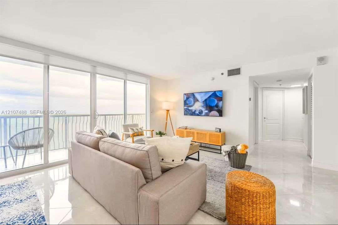 Expansive living area featuring floor-to-ceiling glass sliding doors, stone-finish tile flooring, and a private balcony with metal railing