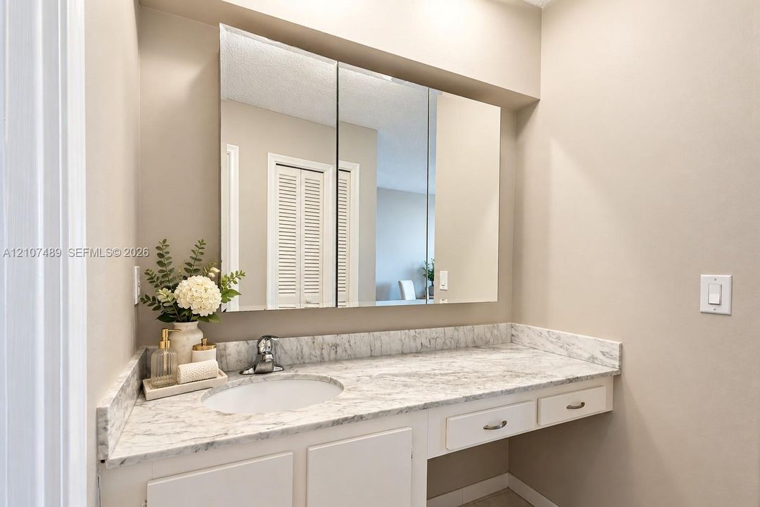 Vanity featuring a stone-patterned countertop, integrated basin with a chrome faucet, tri-fold mirrored medicine cabinet, and built-in drawers