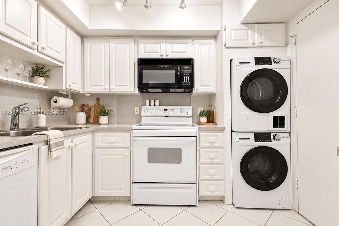 Kitchen featuring shaker-style cabinetry, solid-surface countertops, stainless steel sink with high-arc faucet, integrated laundry center, and tile flooring