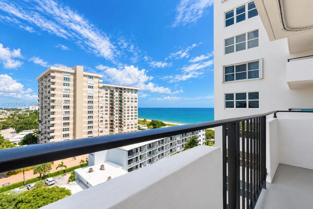 Covered balcony featuring metal railings and concrete flooring with an expanse of ocean and coastline
