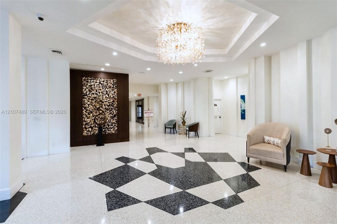 Foyer featuring a recessed tray ceiling with a crystal chandelier, polished stone flooring with geometric inlay, and a dark wood-paneled accent wall