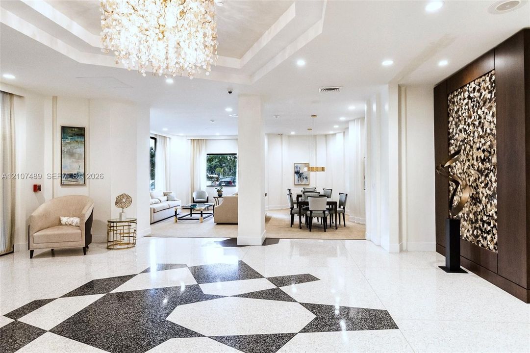 Polished stone flooring featuring a geometric inlay, recessed tray ceiling with a crystal chandelier, and a floor-to-ceiling decorative accent wall with textured paneling