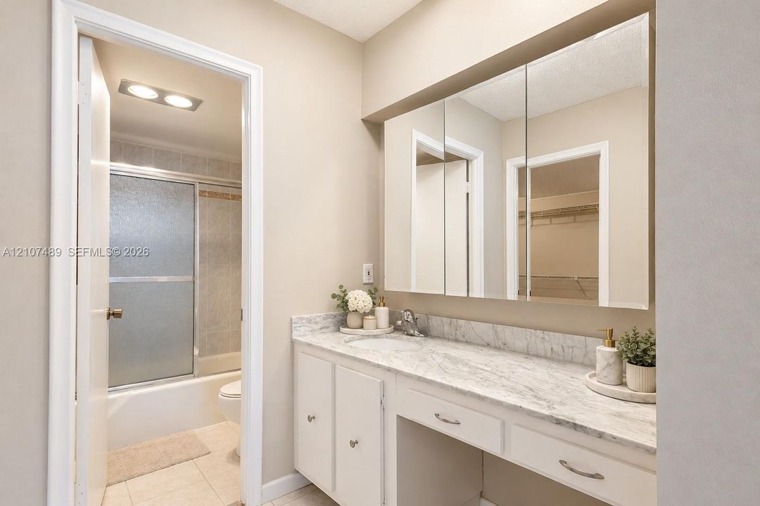 Vanity featuring a stone-look countertop, integrated sink, built-in medicine cabinet, and a dedicated seated vanity space, complete with a separate area containing a tub-shower combination with sliding glass doors