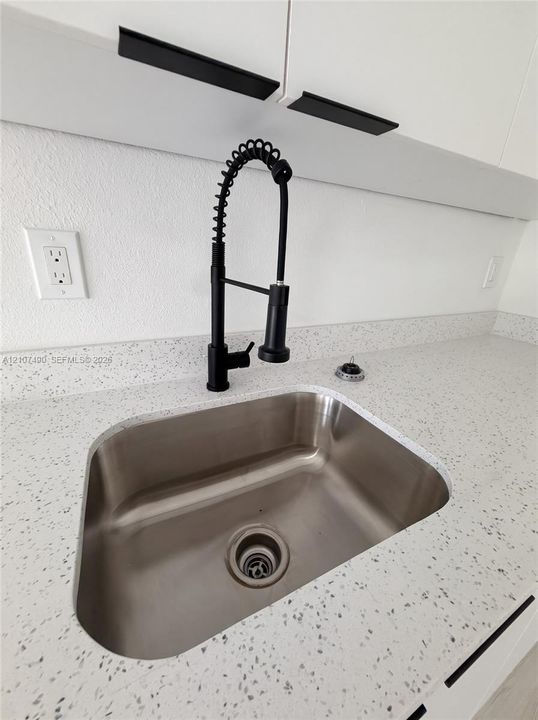 Undermount stainless steel sink featuring a matte black high-arc pull-down faucet, speckled composite countertop, and white cabinetry with matte black linear hardware