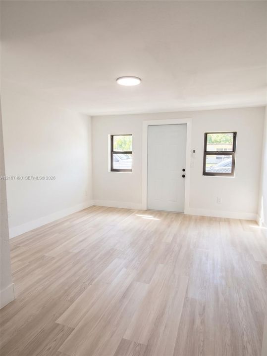 Spacious Interior space featuring light-toned wood-finish flooring, neutral wall paint, two windows with dark frames, and a solid-core entry door