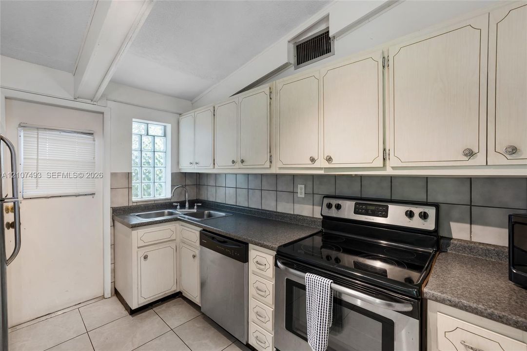 Main Apt, East side, Kitchen featuring white cabinetry, dark stone-finish countertops, stainless steel appliances, a square glass block window, and tile flooring