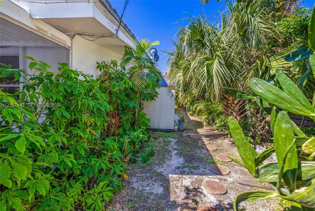 East side, Exterior side yard featuring a series of circular stone pavers and mature tropical landscaping including palm trees
