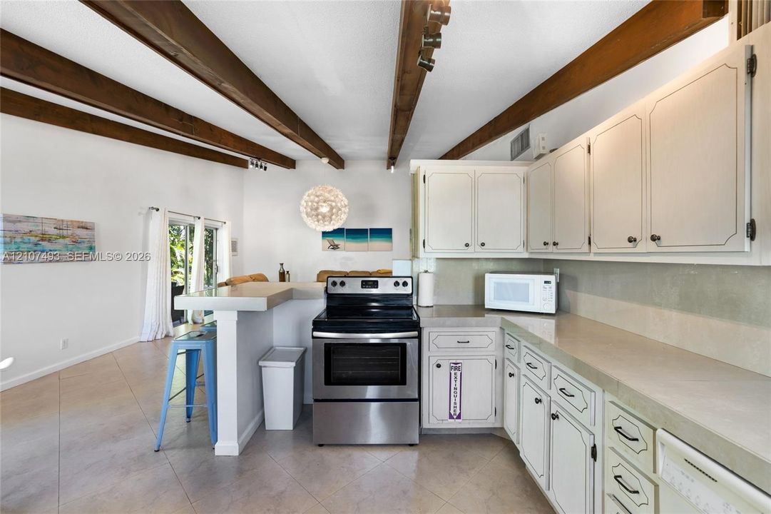 Main Apt, West side, Kitchen featuring exposed wood ceiling beams, solid-surface countertops, white cabinetry, and stainless steel range