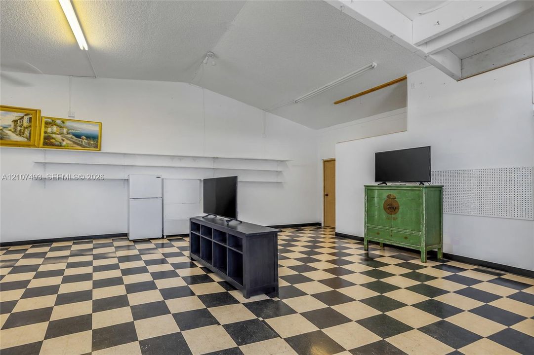 Property interior garage space, Interior space featuring vaulted ceilings, high-contrast checkerboard flooring, linear wall-mounted shelving, and integrated pegboard wall panels