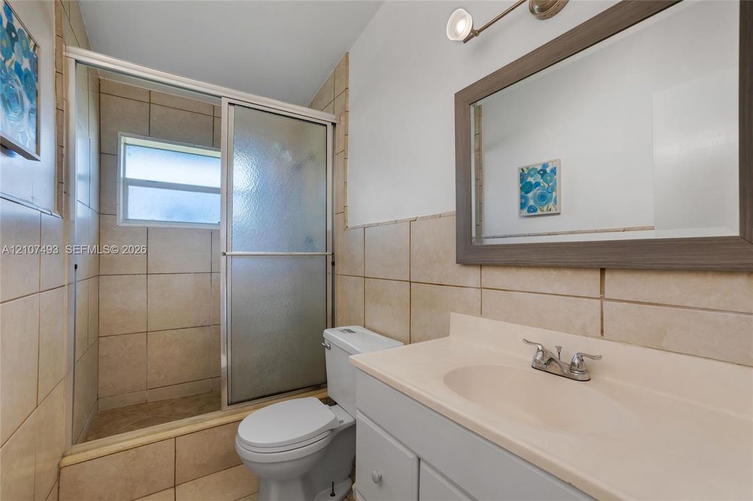 Studio 1, Bathroom featuring a vanity with an integrated basin, a framed wall mirror, a tiled shower enclosure with sliding glass doors, and light-toned wall tile