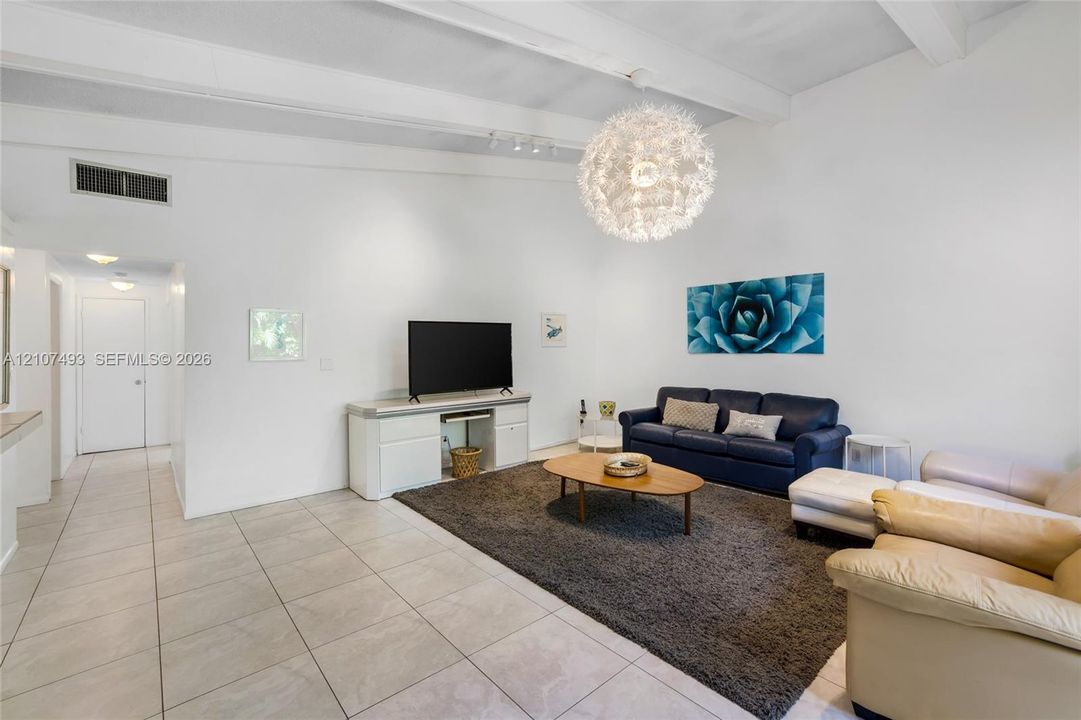 Main Apt, East side, Vaulted ceilings with exposed beams, large spherical chandelier, and ceramic tile flooring