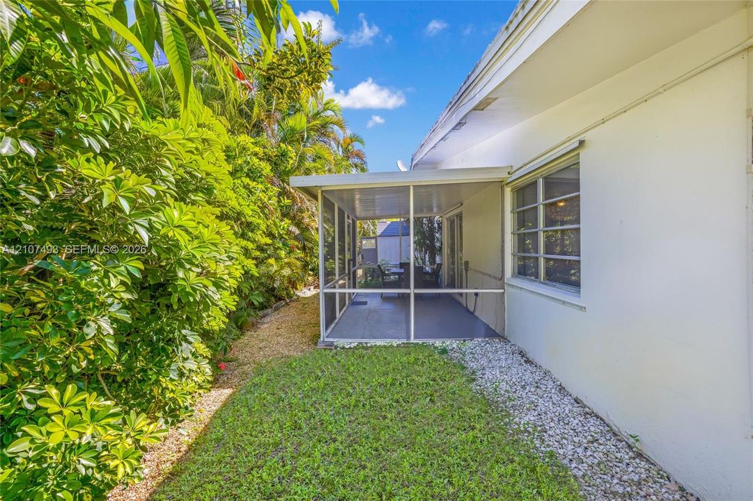 Main Apt, West side, rear Screened-in patio with concrete flooring, manicured lawn, established perimeter hedges, and decorative rock landscaping